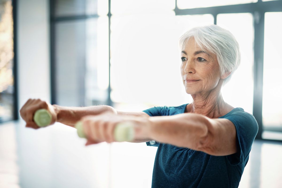 Senior woman carrying lightly weighted dumbbells with arms outstretched in front.