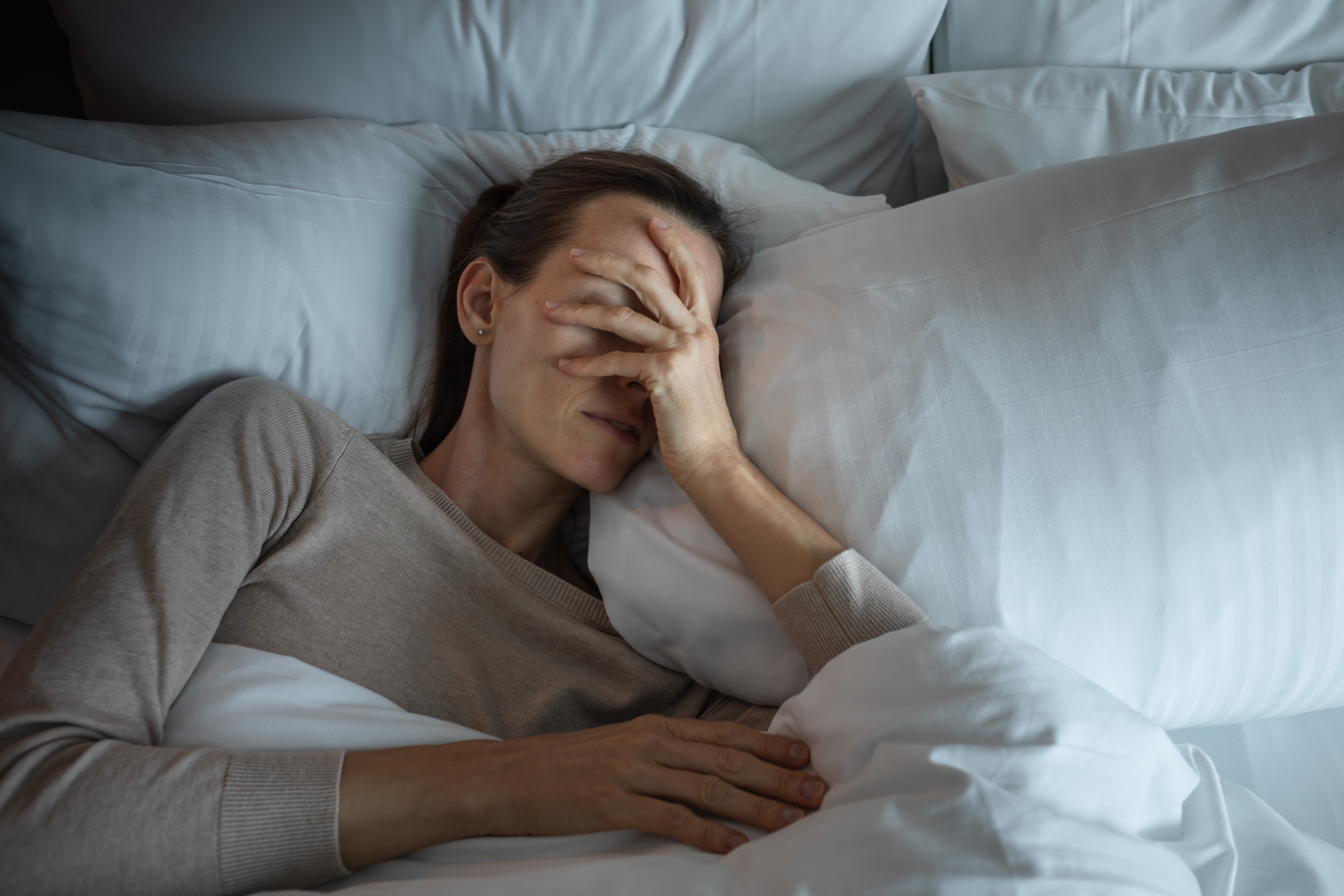 Woman in bed with hands over face suffering from symptoms of a concussion